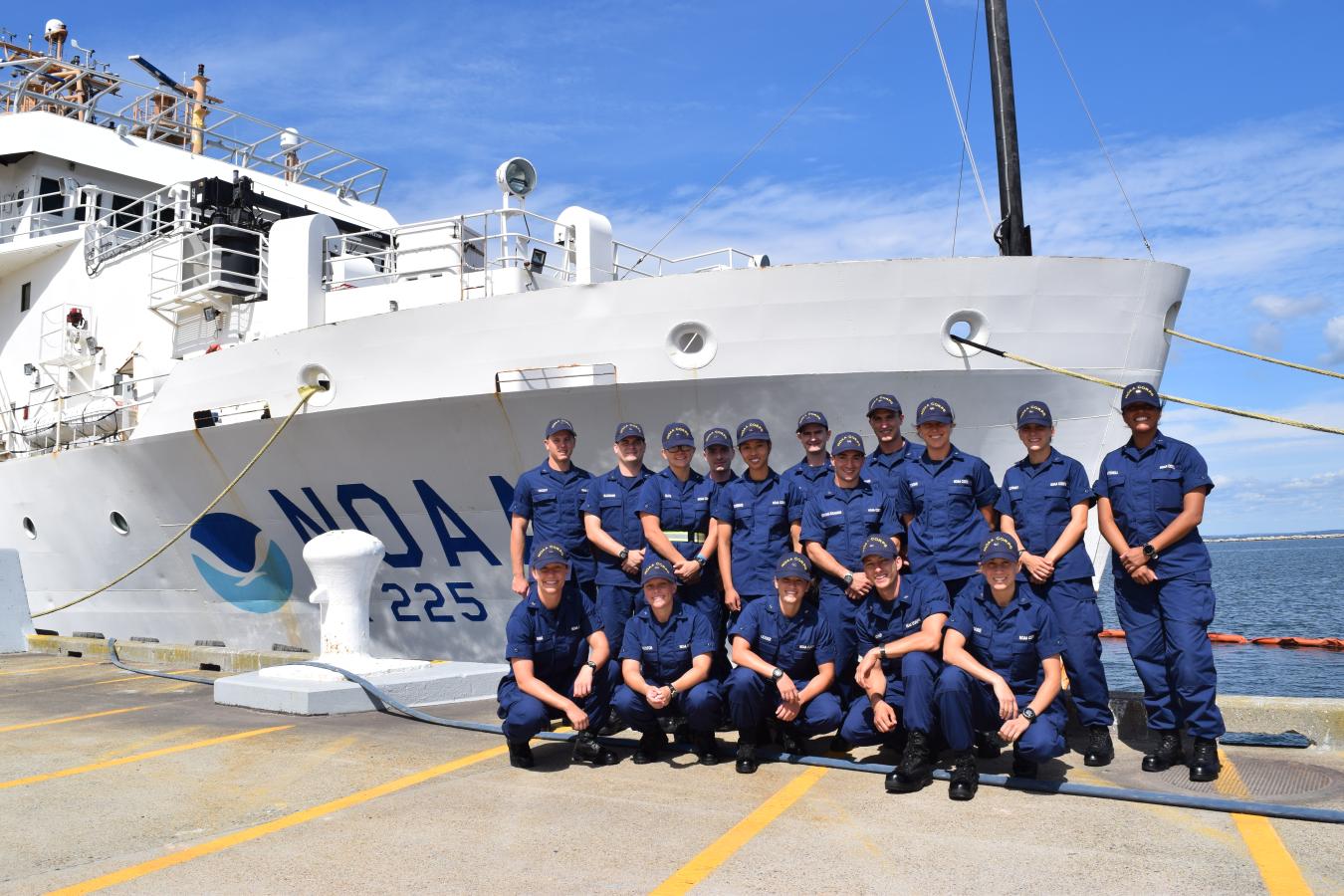 NOAA Corps officer candidates clad in blue uniforms on the pier in front of a white NOAA ship