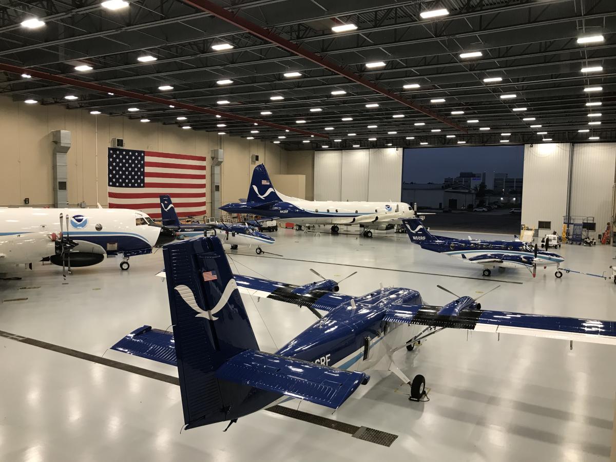 NOAA aircraft in a hangar with the U.S. flag in the background