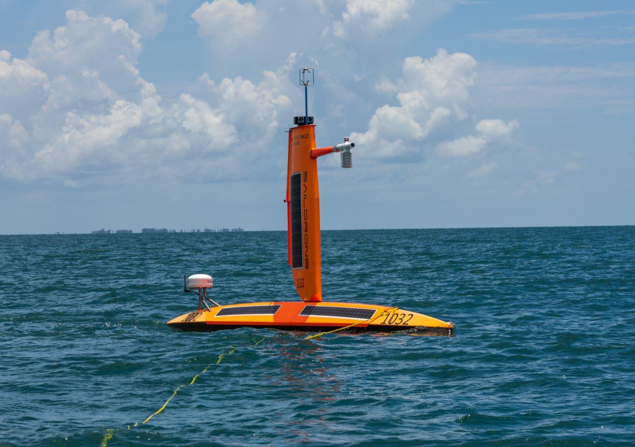 A bright orange uncrewed Saildrone surface vehicle on the water