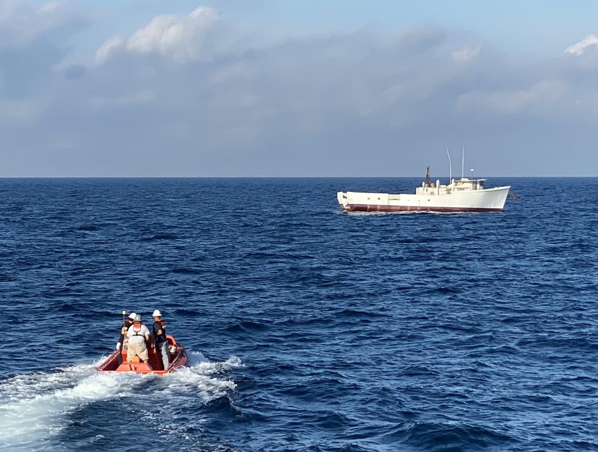 A small boat moves toward a larger boat in the distance