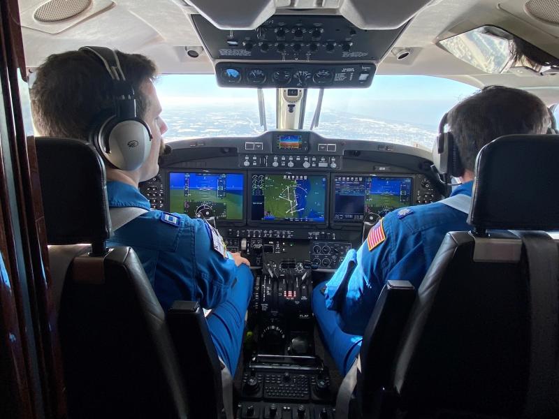 Two pilots in blue flight suits at the controls of a NOAA King Air aircraft