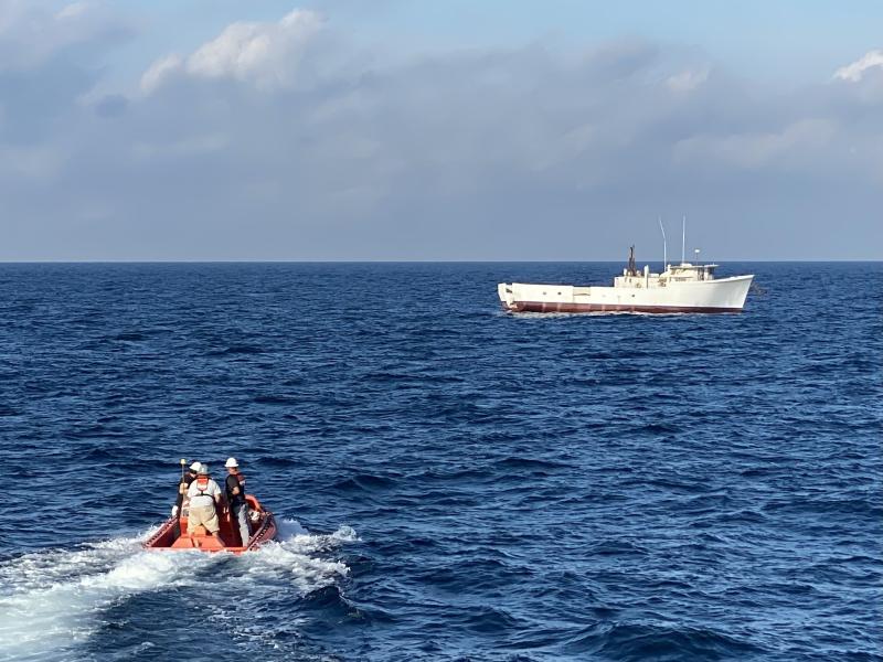 A small boat moves toward a larger boat in the distance