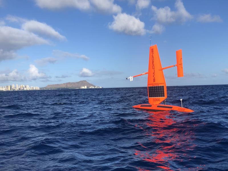 A bright orange Saildrone uncrewed surface vehicle on the water