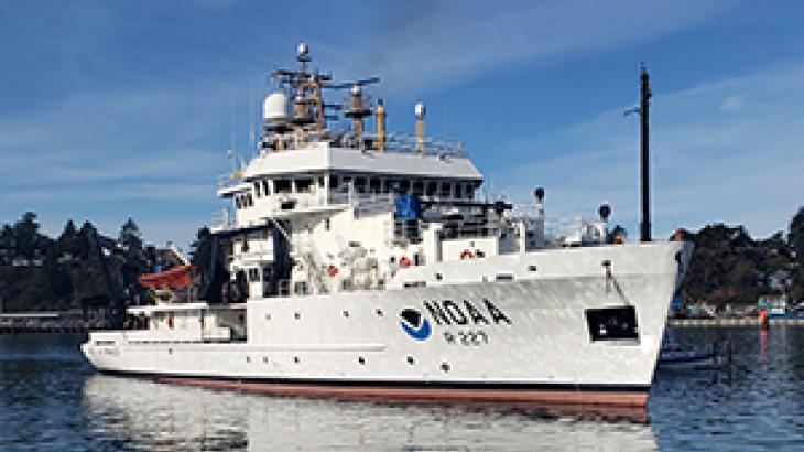 A white NOAA fisheries survey ship under a blue sky