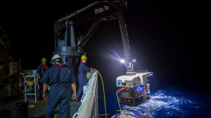 A robot submarine dangling from a ship's crane at night