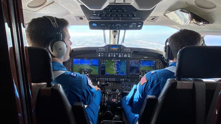 Two pilots in blue flight suits at the controls of a NOAA King Air aircraft