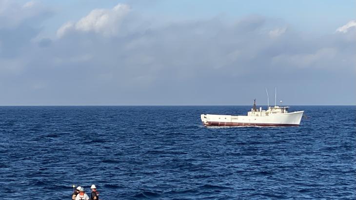 A small boat moves toward a larger boat in the distance