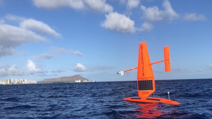 A bright orange Saildrone uncrewed surface vehicle on the water