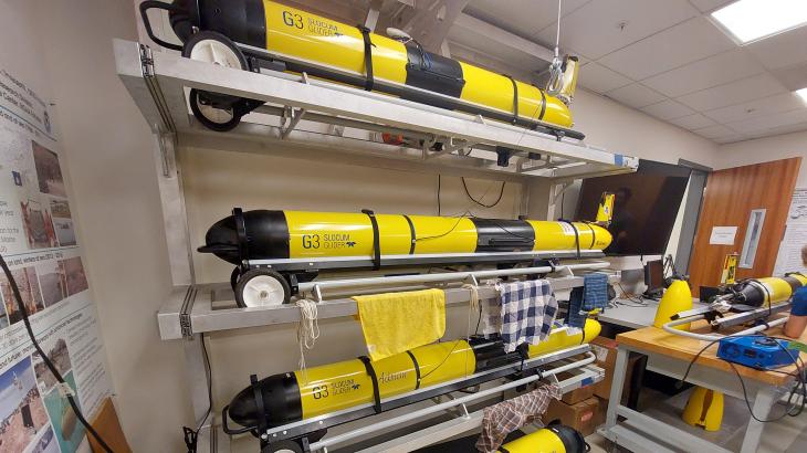 Multiple yellow Slocum gliders in their racks in a science lab.