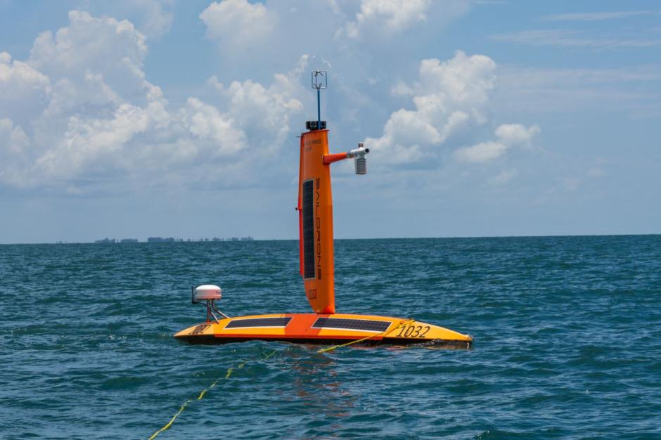 A bright orange uncrewed Saildrone surface vehicle on the water