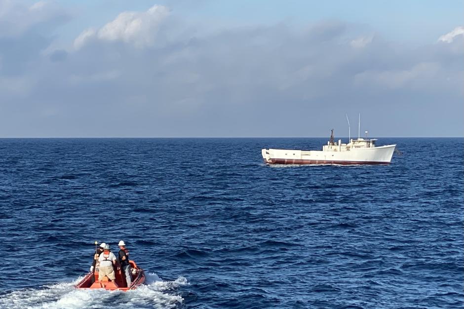 A small boat moves toward a larger boat in the distance