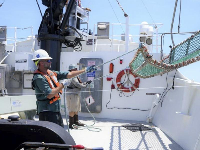 Two crew members aboard a white NOAA ship pull in a mesh cradle