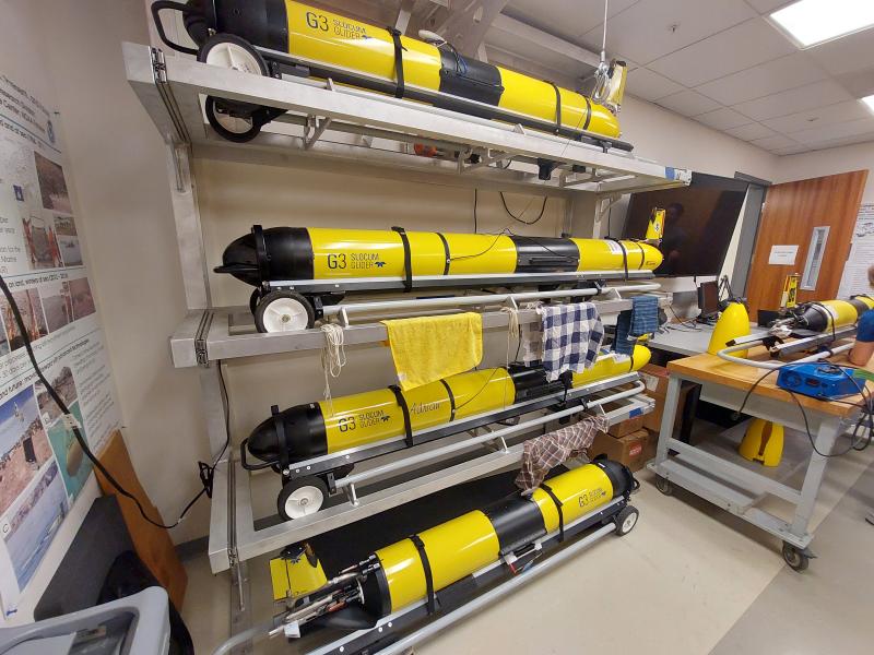 Multiple yellow Slocum gliders in their racks in a science lab.