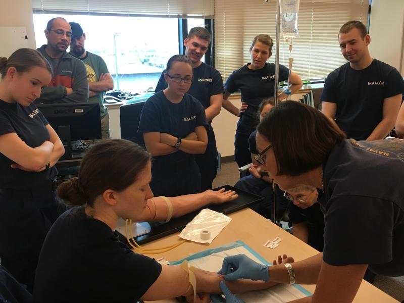 People watching a medical professional insert an I.V. into someone's arm. 