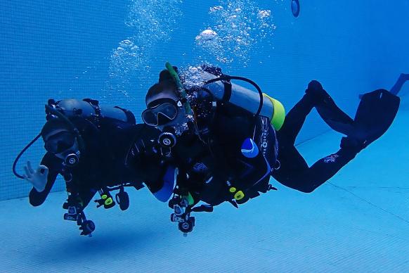 A pair of NOAA scuba dives under water in a swimming pool