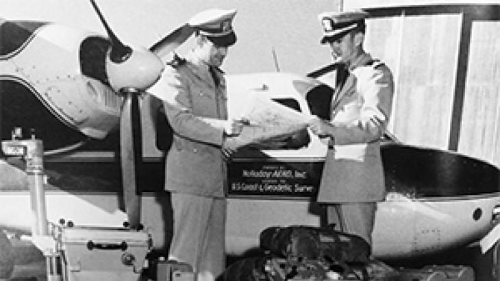 Two male uniformed officers standing next to a twin-engine airplane in 1956