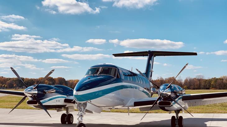 A small blue and white turboprop on the tarmac on sunny day