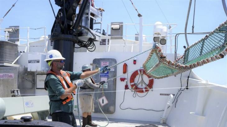 Two crew members aboard a white NOAA ship pull in a mesh cradle