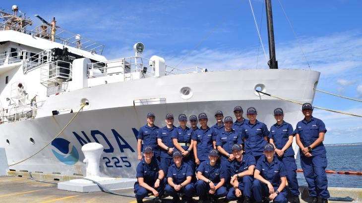 NOAA Corps officer candidates clad in blue uniforms on the pier in front of a white NOAA ship