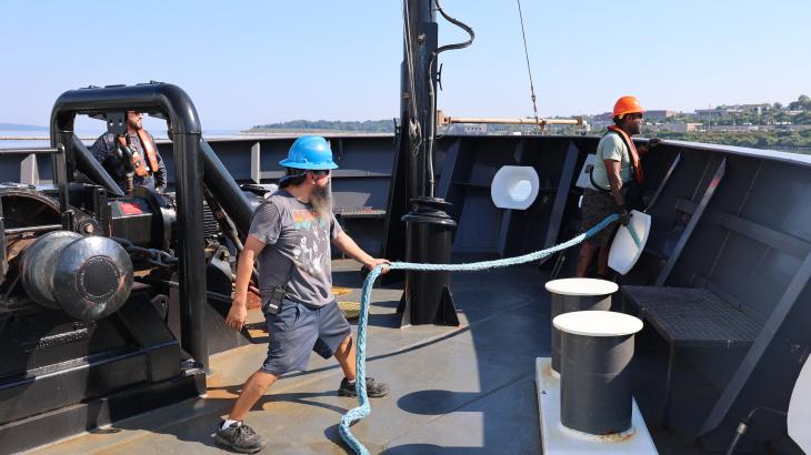 Two crew members handle mooring lines at a ship's bow