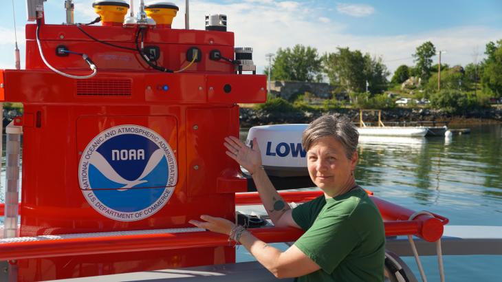 A woman pointing to an orange uncrewed surface vehicle