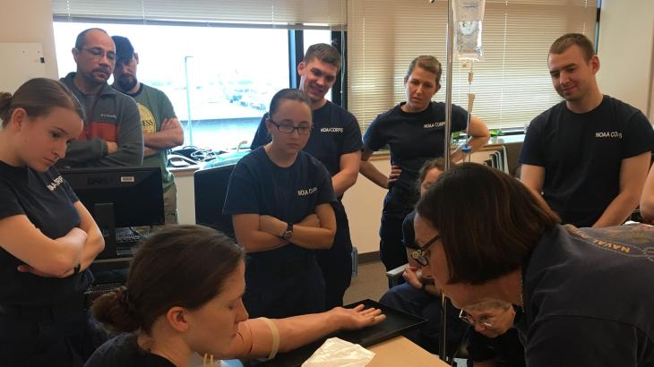 People watching a medical professional insert an I.V. into someone's arm. 