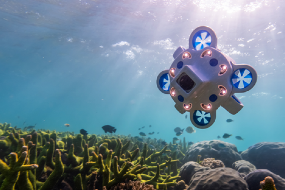 A blue and white Hydrus autonomous underwater vehicle transits underwater over the sea floor.